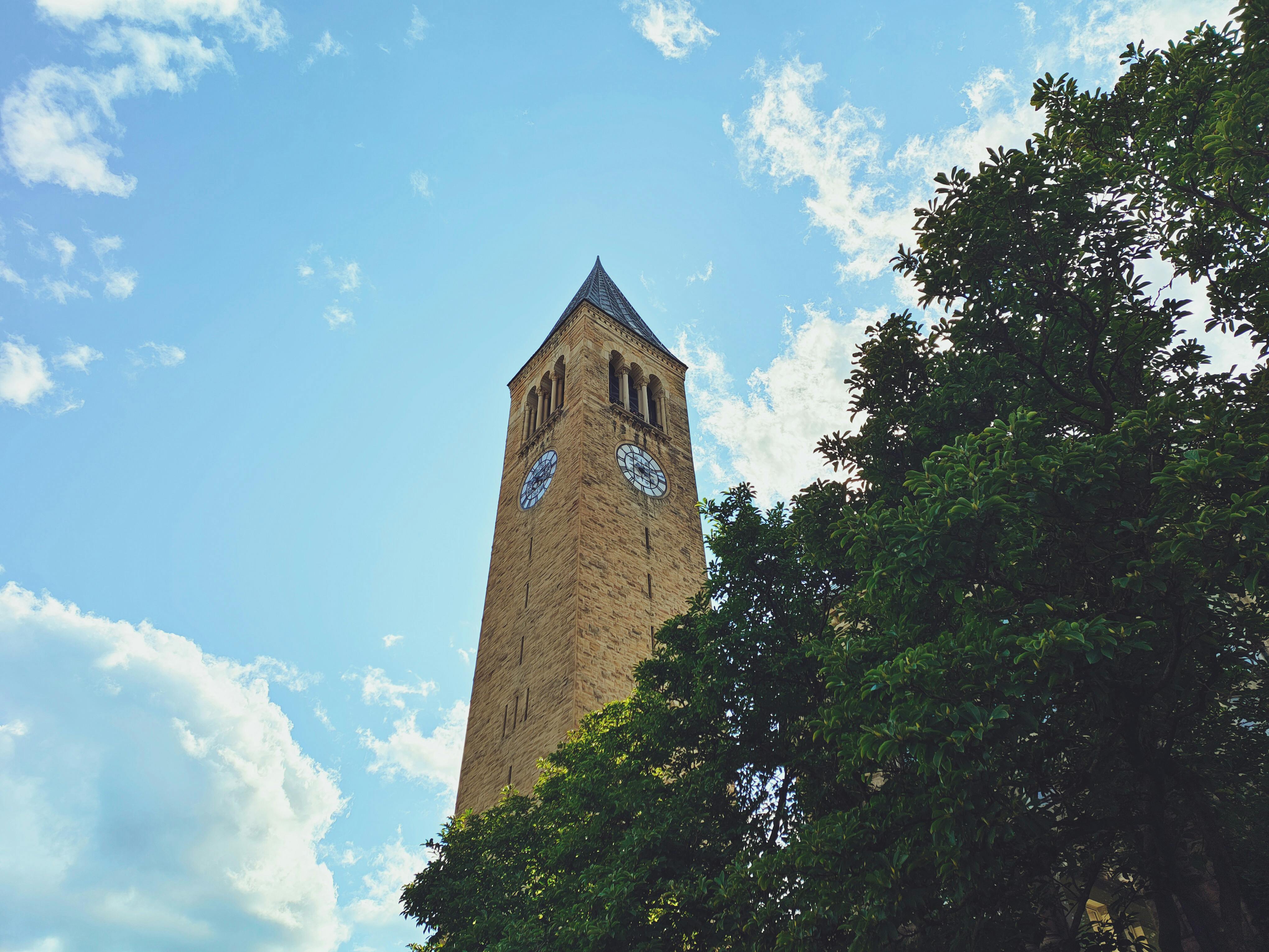 Low angle view of McGraw Tower at Cornell University in Ithaca, with clear blue skies and trees.